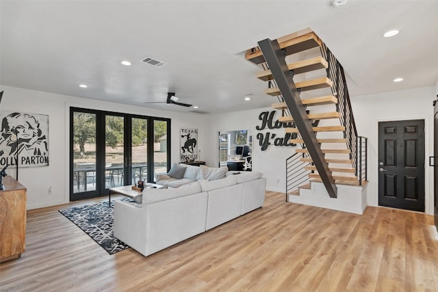 living room featuring ceiling fan, a barn door, french doors, and light hardwood / wood-style flooring