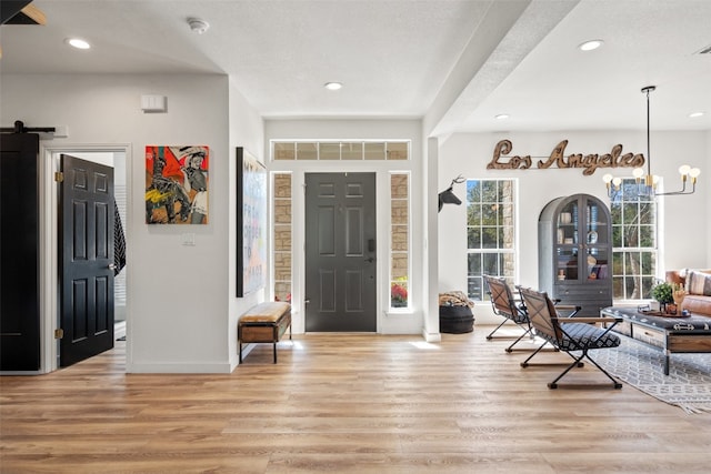 foyer featuring light hardwood / wood-style floors, a barn door, and a chandelier