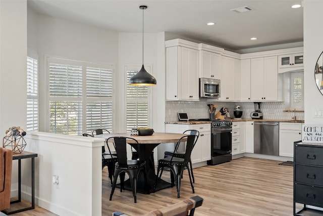 kitchen with light hardwood / wood-style floors, white cabinetry, stainless steel appliances, and hanging light fixtures