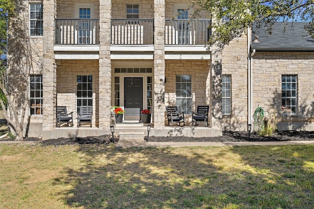 view of exterior entry featuring a lawn and a balcony