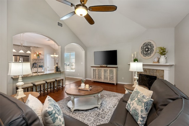 living room with ceiling fan with notable chandelier, lofted ceiling, dark wood-type flooring, and a tiled fireplace