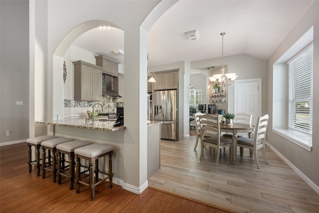 interior space featuring pendant lighting, wall chimney exhaust hood, stainless steel fridge, tasteful backsplash, and light hardwood / wood-style floors