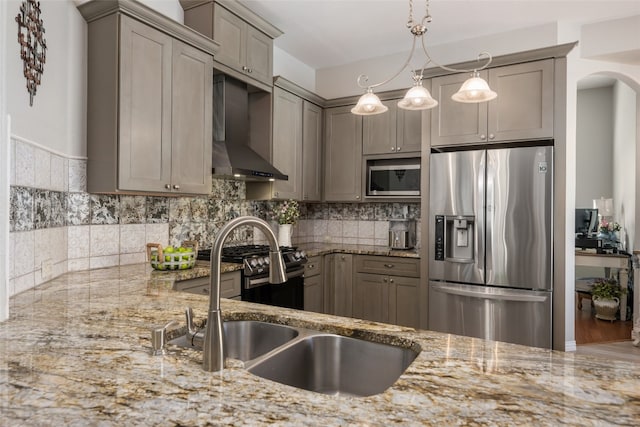 kitchen with appliances with stainless steel finishes, light stone counters, wall chimney exhaust hood, sink, and hanging light fixtures