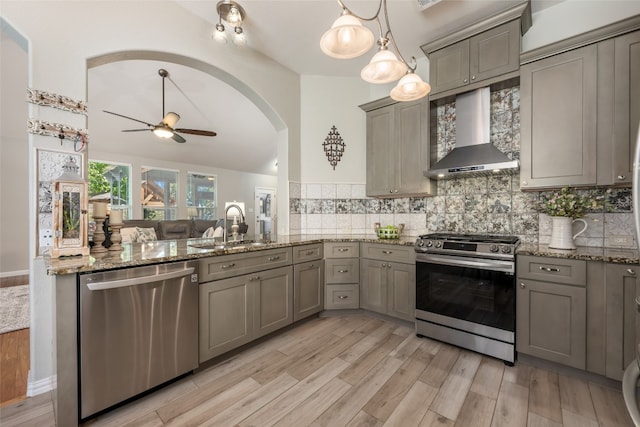 kitchen featuring sink, wall chimney exhaust hood, pendant lighting, appliances with stainless steel finishes, and light wood-type flooring