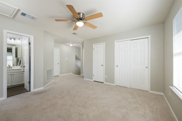 unfurnished bedroom featuring ceiling fan, two closets, light carpet, and ensuite bath