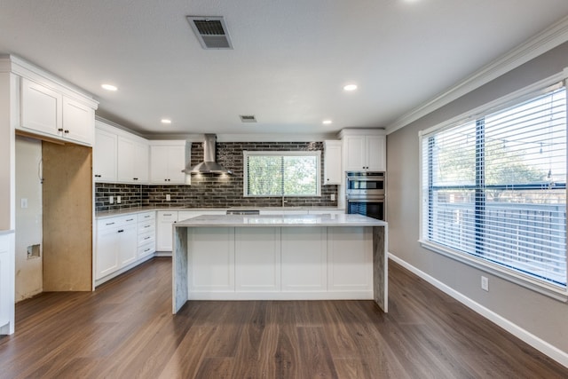 kitchen featuring white cabinets, crown molding, and wall chimney range hood