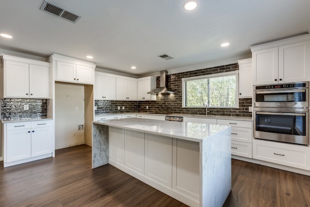 kitchen featuring wall chimney exhaust hood, dark hardwood / wood-style floors, light stone counters, white cabinetry, and stainless steel appliances