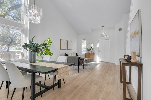 dining area with a notable chandelier, light hardwood / wood-style flooring, and a high ceiling