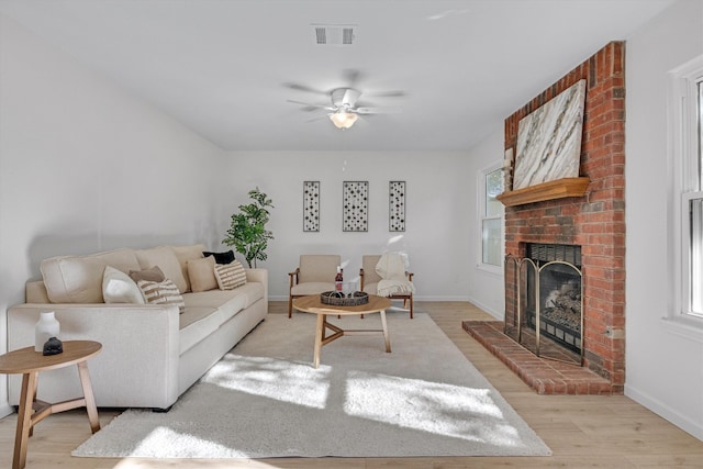 living room featuring ceiling fan, a brick fireplace, and light wood-type flooring