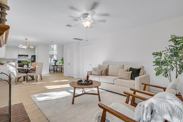 living room with ceiling fan with notable chandelier and light hardwood / wood-style floors