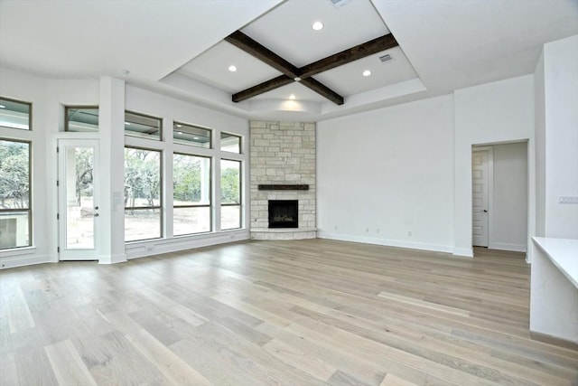 unfurnished living room with beamed ceiling, coffered ceiling, light hardwood / wood-style floors, and a stone fireplace