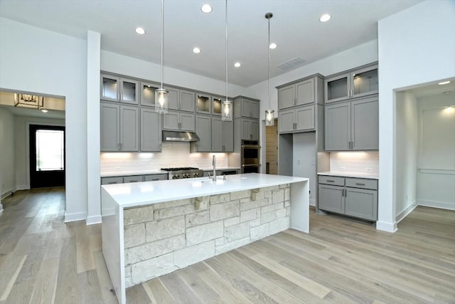 kitchen with tasteful backsplash, hanging light fixtures, and a center island with sink