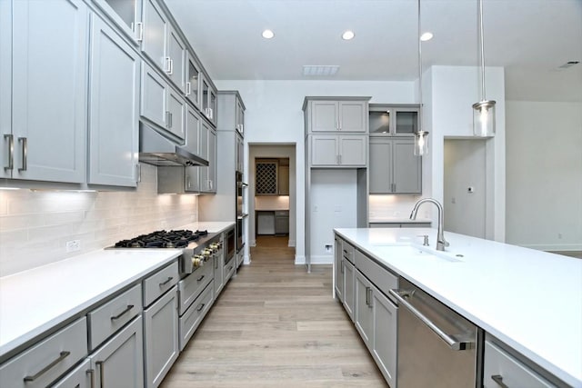 kitchen featuring sink, stainless steel appliances, decorative backsplash, decorative light fixtures, and light wood-type flooring