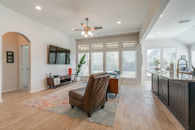 living room with sink, vaulted ceiling, ceiling fan, a textured ceiling, and light hardwood / wood-style floors