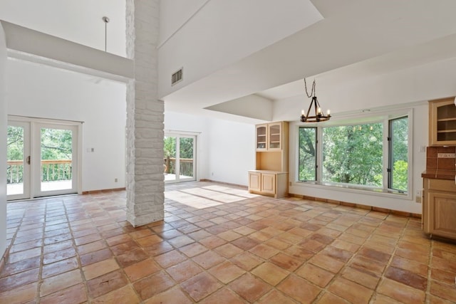 unfurnished living room featuring a notable chandelier, plenty of natural light, and a towering ceiling