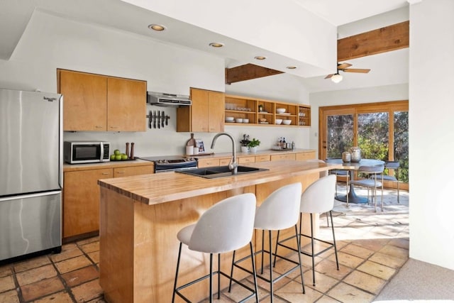 kitchen featuring wood counters, stainless steel appliances, a kitchen island with sink, sink, and range hood