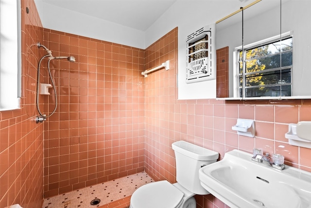 bathroom featuring a tile shower, toilet, tile walls, and sink