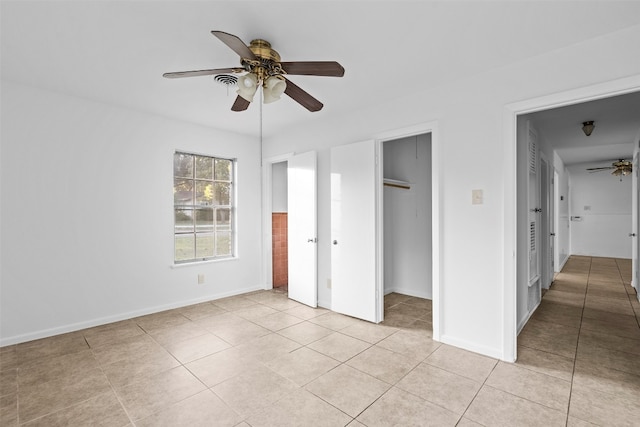 unfurnished bedroom with light tile patterned floors, a spacious closet, and ceiling fan