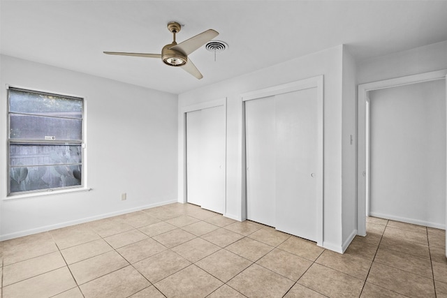 unfurnished bedroom featuring ceiling fan, light tile patterned floors, and multiple closets