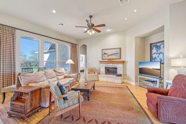 living room featuring a stone fireplace, ceiling fan, and light hardwood / wood-style flooring