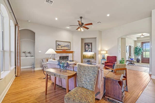 living room with a stone fireplace, ceiling fan, and light hardwood / wood-style flooring