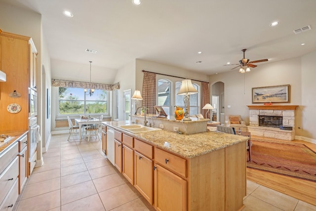 kitchen with a stone fireplace, sink, hanging light fixtures, light tile patterned floors, and an island with sink