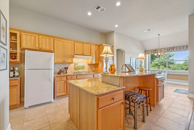 kitchen with a breakfast bar, backsplash, vaulted ceiling, an island with sink, and white fridge