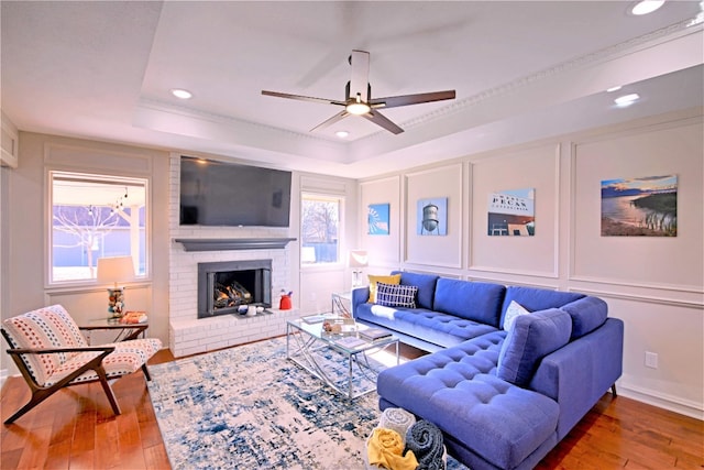 living room featuring hardwood / wood-style flooring, ceiling fan, a raised ceiling, and a brick fireplace