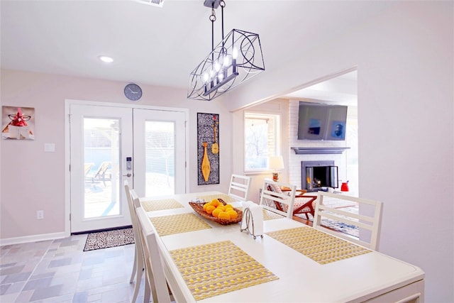 dining area with a notable chandelier, french doors, and a brick fireplace