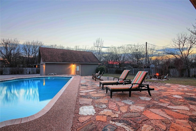 pool at dusk with a patio area and an outdoor structure