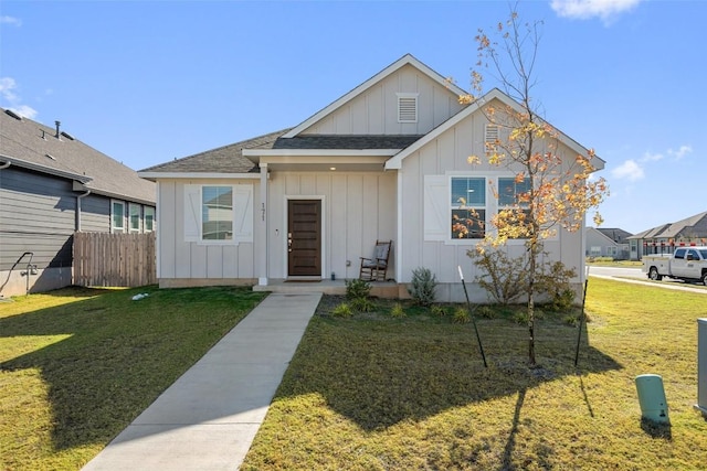 view of front of home featuring a shingled roof, fence, board and batten siding, and a front yard