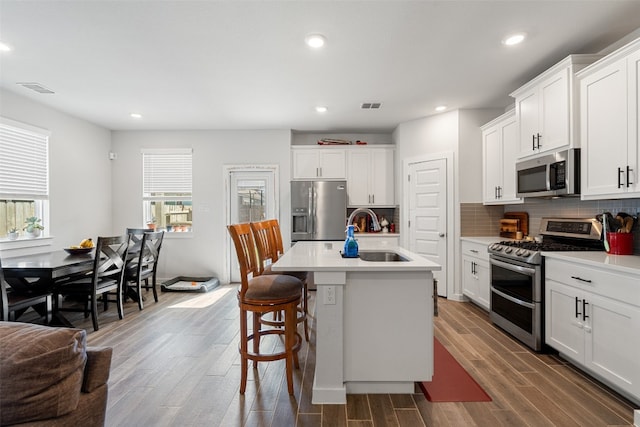 kitchen with sink, stainless steel appliances, a wealth of natural light, and an island with sink