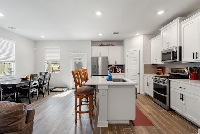 kitchen featuring wood finish floors, a sink, backsplash, stainless steel appliances, and light countertops