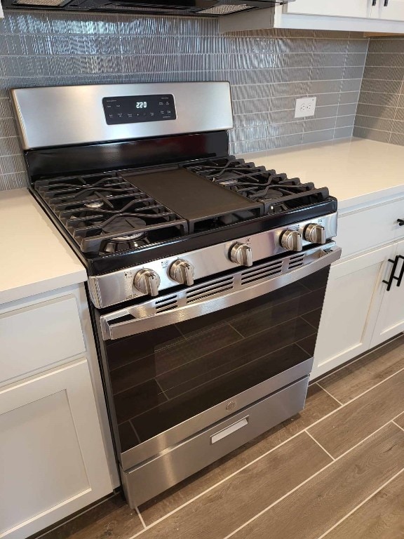 kitchen with decorative backsplash, white cabinets, dark wood-type flooring, and stainless steel gas range