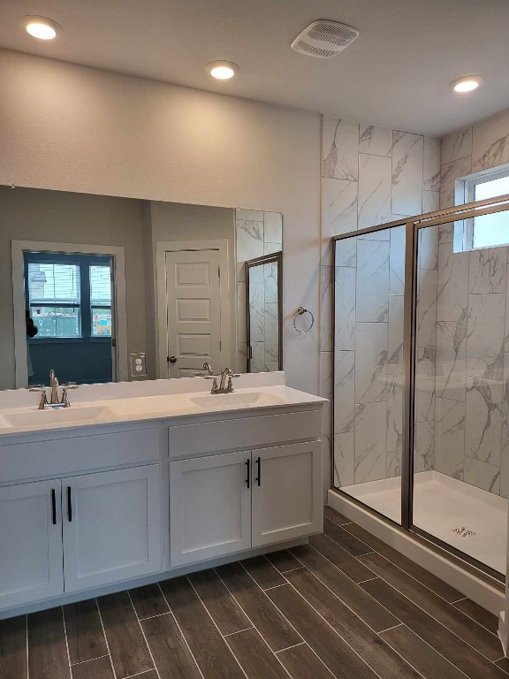 bathroom featuring a marble finish shower, visible vents, wood tiled floor, and a sink