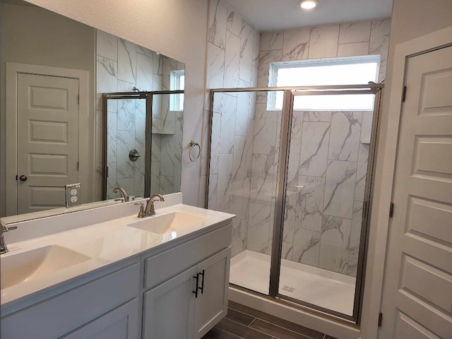 full bath featuring a marble finish shower, double vanity, and a sink