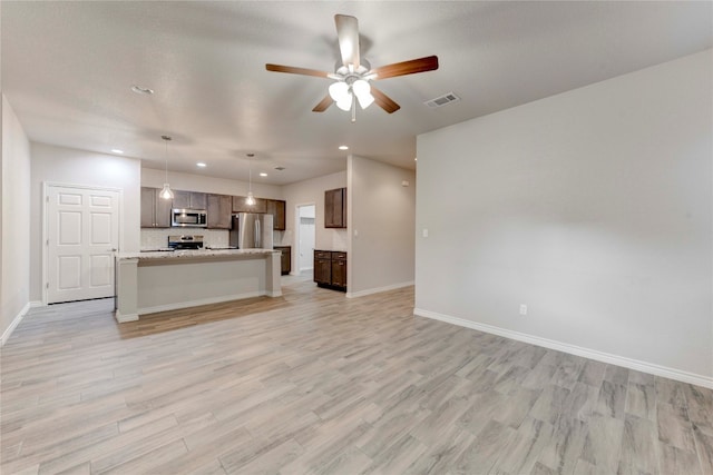 kitchen with ceiling fan, stainless steel appliances, light hardwood / wood-style flooring, pendant lighting, and a center island with sink