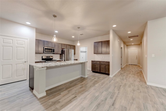 kitchen with pendant lighting, tasteful backsplash, stainless steel appliances, and an island with sink