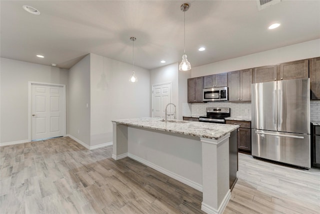 kitchen featuring pendant lighting, light stone countertops, a kitchen island with sink, and appliances with stainless steel finishes