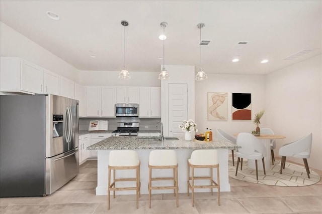 kitchen featuring pendant lighting, a breakfast bar area, appliances with stainless steel finishes, white cabinetry, and a kitchen island with sink