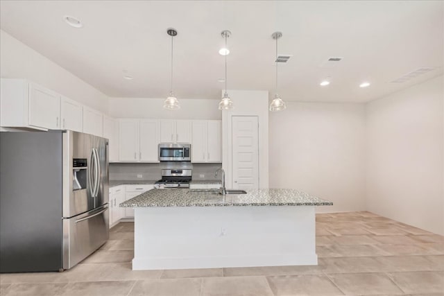 kitchen with decorative light fixtures, white cabinetry, stainless steel appliances, light stone countertops, and a center island with sink