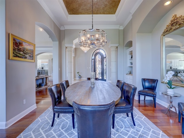 dining room featuring built in features, hardwood / wood-style floors, a raised ceiling, and ornate columns