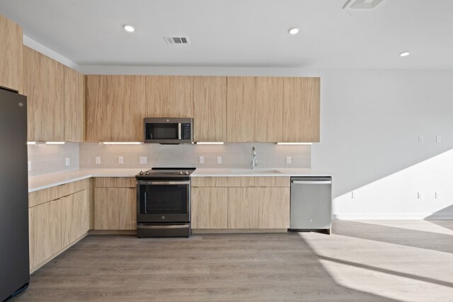 kitchen with backsplash, stainless steel appliances, sink, light brown cabinets, and light hardwood / wood-style floors