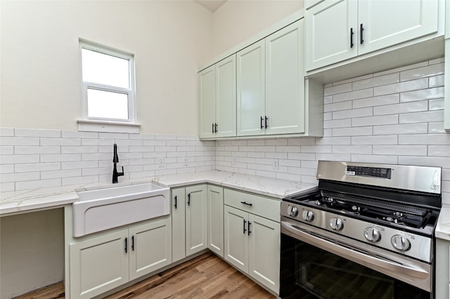 kitchen featuring light wood-type flooring, backsplash, light stone counters, gas range, and sink