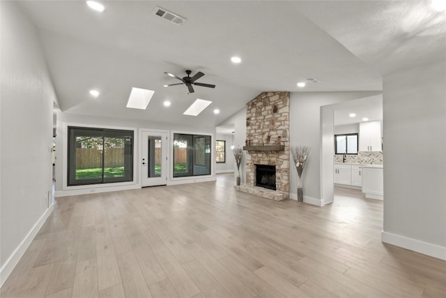 unfurnished living room featuring ceiling fan, lofted ceiling with skylight, a fireplace, and light hardwood / wood-style flooring