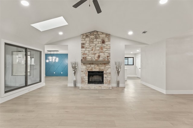 unfurnished living room featuring a fireplace, ceiling fan with notable chandelier, light hardwood / wood-style floors, and lofted ceiling with skylight