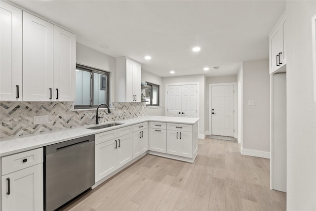 kitchen with light wood-type flooring, tasteful backsplash, stainless steel dishwasher, sink, and white cabinets