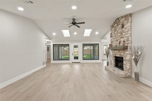 unfurnished living room with light wood-type flooring, a stone fireplace, ceiling fan, and vaulted ceiling with skylight