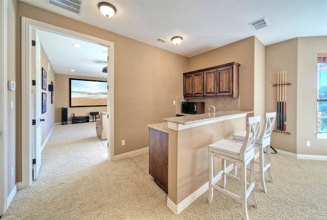 kitchen featuring light stone countertops, a kitchen breakfast bar, light colored carpet, and kitchen peninsula