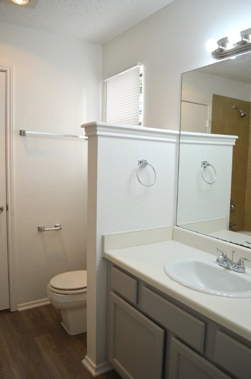 bathroom with a tile shower, a textured ceiling, vanity, wood-type flooring, and toilet